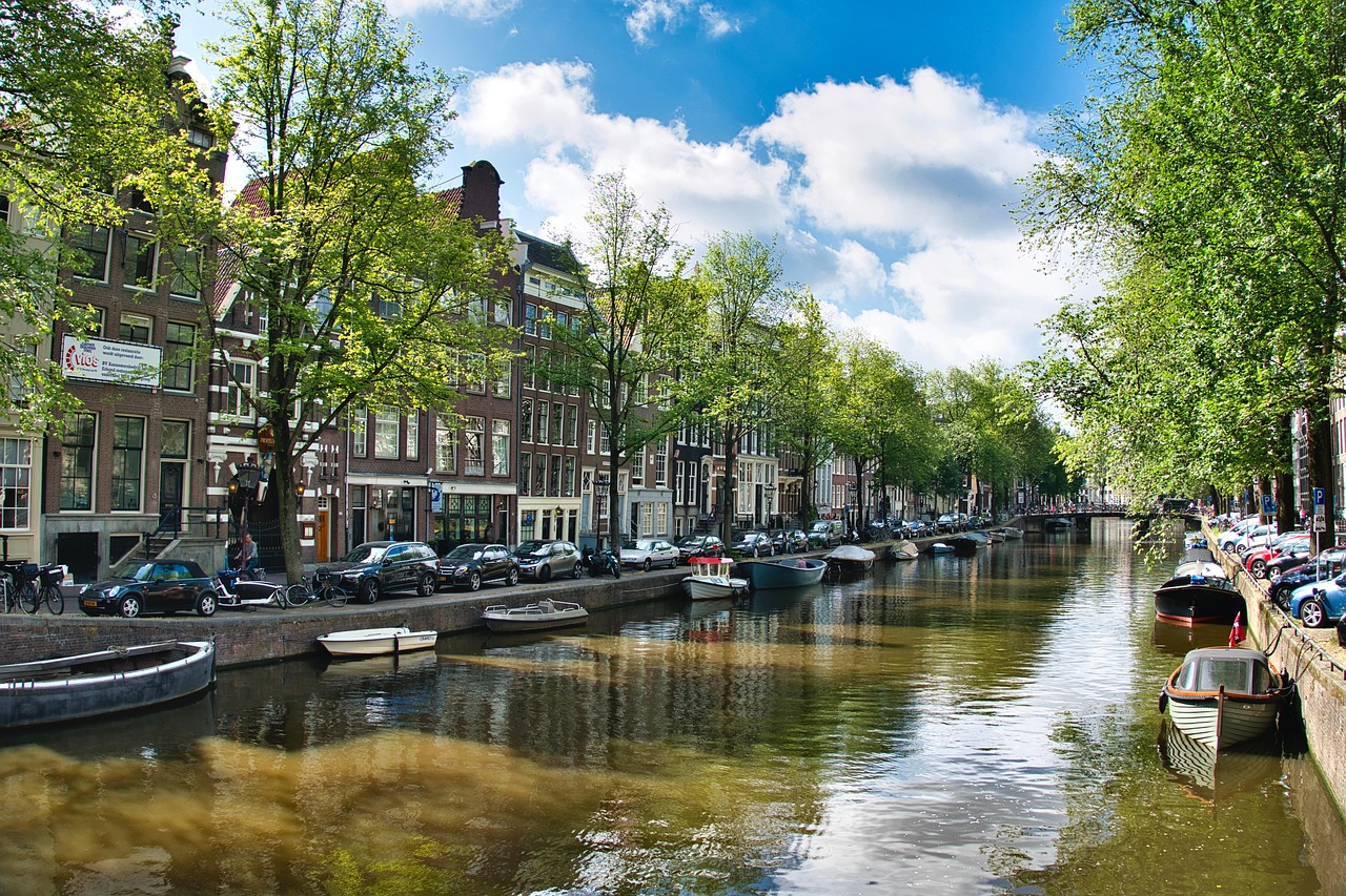 Amsterdam canal street with parked cars and boats