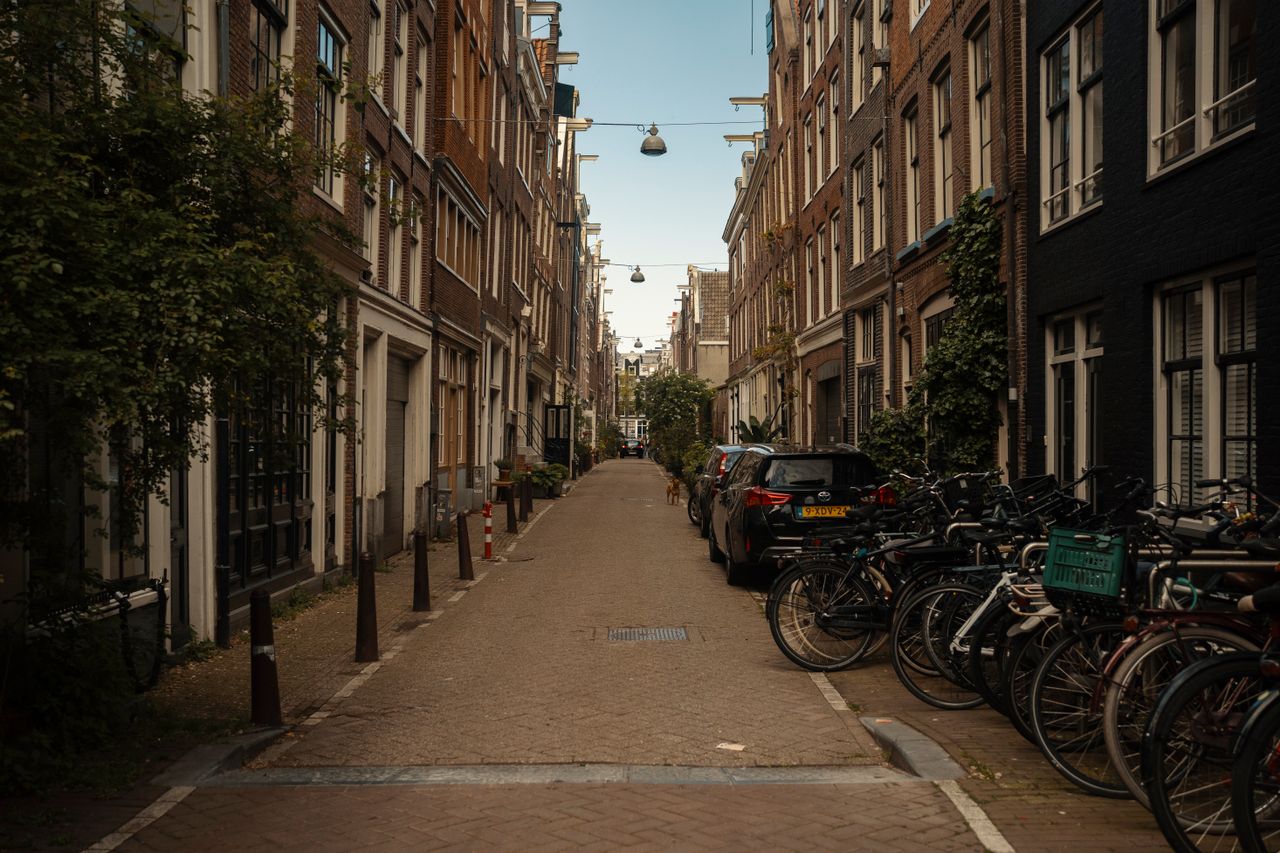 Geparkeerde fietsen en auto’s naast elkaar in een smalle Amsterdamse straat